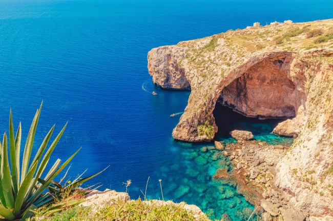Tourist boat passing through the natural rock arch at the Blue Grotto, Malta